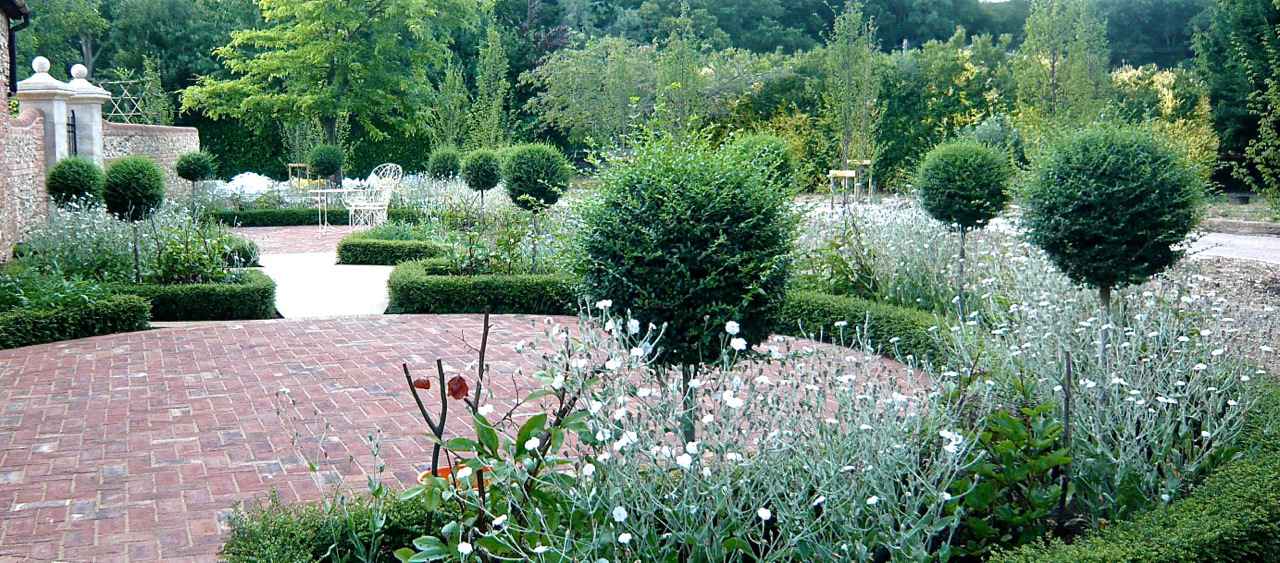 This is a walled garden with lots of pompom topiary, white frothy planting & herringbone brick paving