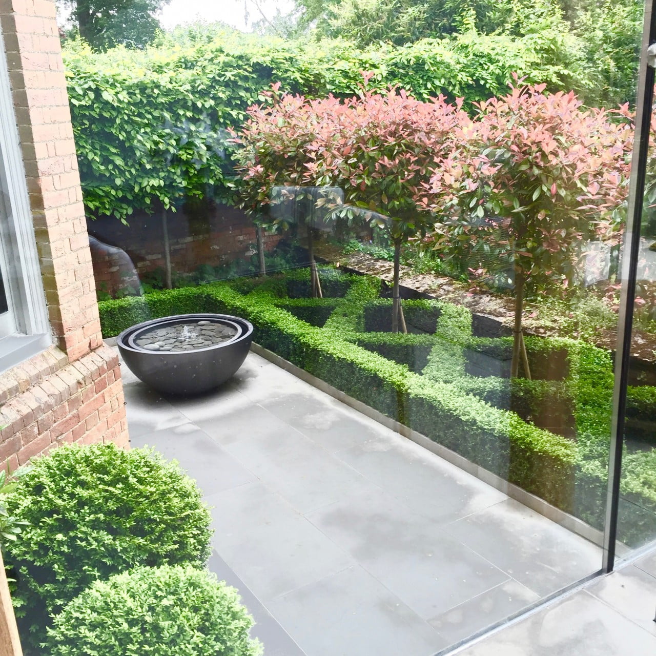 A view from our glass box extension down to our small formal courtyard garden with water feature & pleached hornbeam trees