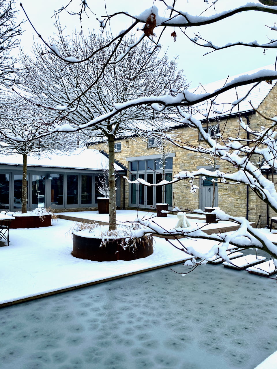 view across the frozen pond to the Cotswold barn beyond. Garden design by Cotswold garden designer Jo Alderson Phillips